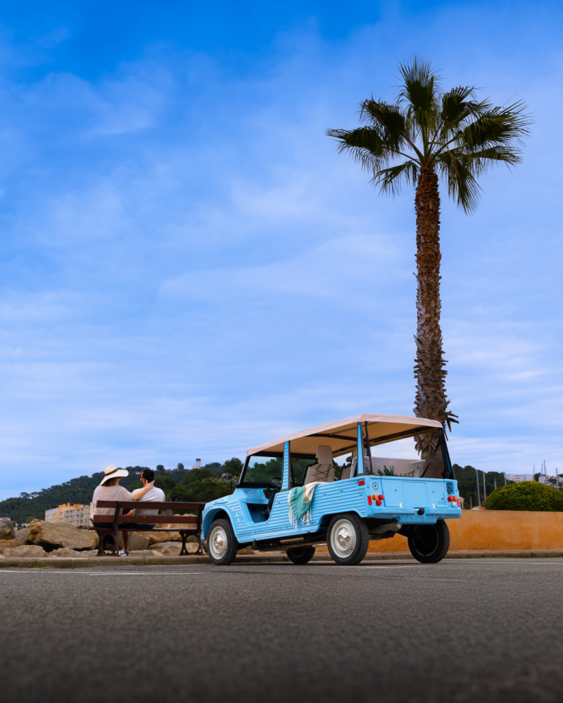 eStory Méhari électrique vue de dos garée à Monaco avec couple sur banc et palmier